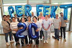 Ein Foto von einer Gruppe von Menschen, die in der Hand Luftballons halte, die das Wort "Perfekt" und die Zahl 20 ergeben.