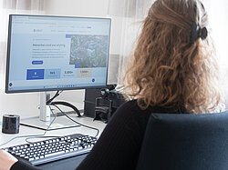 Eine Frau sitzt vor einem PC Bildschirm, geöffnet ist die neue Internetseite.
